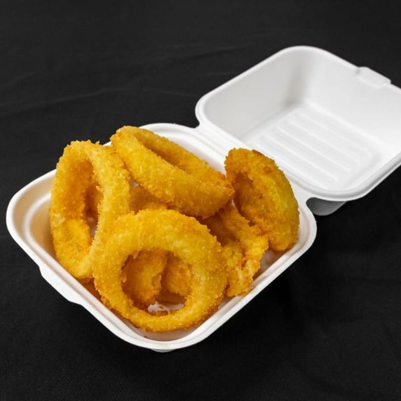 Golden-brown onion rings in a white Mother & Daughter Kitchen takeout container on a dark background.