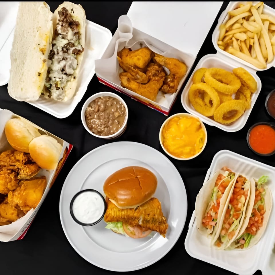 An overhead view of various fast-food items, including a cheesesteak, fried chicken, fries, onion rings, tacos, and a fish sandwich.