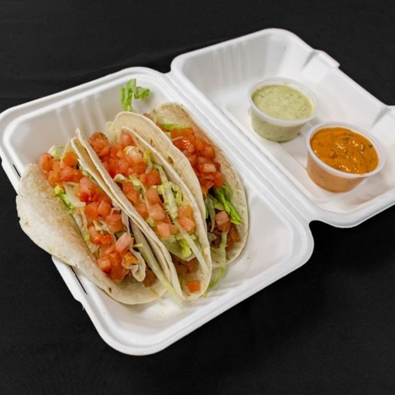 Three Mother & Daughter Kitchen tacos with lettuce and tomato, plus two dipping sauces in a takeout container.